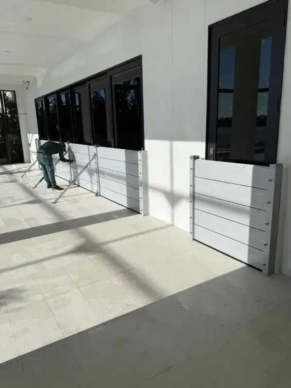 Aluminum flood barrier panels installed along sliding glass doors on a covered patio in Fort Myers Florida with technician securing support brackets